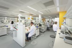 some people in white lab coats working on computers and other equipment with yellow walls behind them