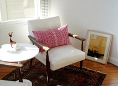 a living room with a white chair, table and pictures on the wall next to it