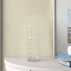 a vase sitting on top of a white table next to a book and framed photograph