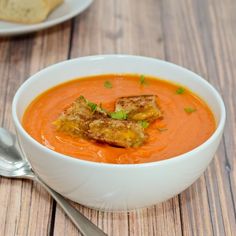 a white bowl filled with carrot soup on top of a wooden table next to bread