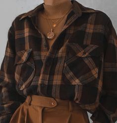 a woman wearing a brown and black plaid shirt with a gold necklace on her neck