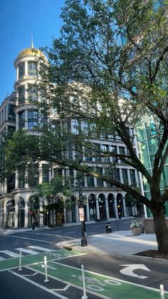 a large white building sitting next to a tree on the side of a city street