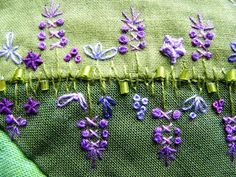 some purple flowers are on the side of a green piece of cloth with yellow pins