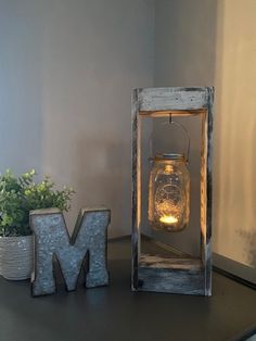 a small lantern is sitting on a table next to a letter m and a potted plant