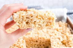 a hand holding a piece of rice krispy kreme on top of a pan