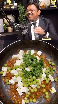 a man in a suit and tie holding a microphone next to a frying pan filled with food