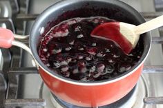 a red pot filled with blueberries and sauce on top of a stove next to a wooden spatula