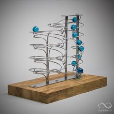 a metal sculpture with blue balls on it's sides and a wooden block in the foreground