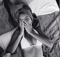 a woman covers her face with a towel while laying in bed next to a pillow