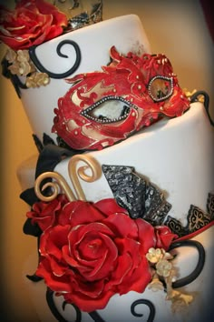 two tiered cake decorated with red and black masquerades, roses and leaves