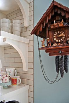 a wooden cuckoo clock hanging from the side of a wall next to cups and mugs