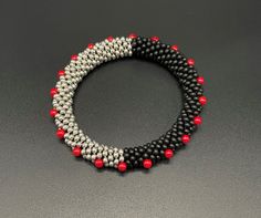 two bracelets with red and black beads on a gray surface, one has a silver beaded clasp