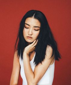 a woman with long black hair and white tank top is looking down at her hand