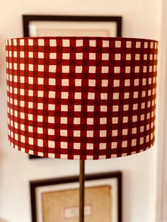 a red and white checkered lamp shade sitting on top of a table next to framed pictures