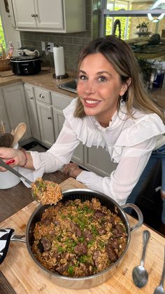 a woman is holding a spoon over a pan full of food on a kitchen counter