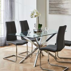 a glass dining table with four chairs and a vase filled with flowers on the side