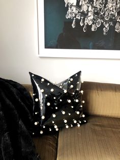 a black and white polka dot pillow sitting on top of a brown couch next to a painting