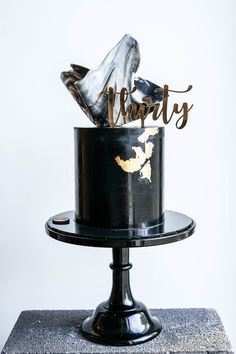 a black and white cake with gold foil on top that reads thirty fifty, sitting on a pedestal