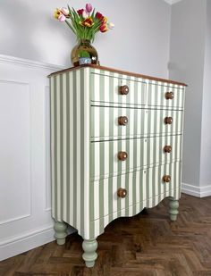 a striped chest of drawers with flowers in a vase sitting on it's top