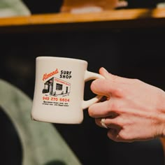 a person holding a coffee mug in their hand with the words almonds surf shop on it