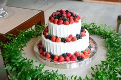 a three tiered cake with fresh berries on top and greenery around the edges