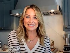 a woman is smiling in the kitchen with blue cabinets and silver appliances behind her she is wearing a black and white striped sweater