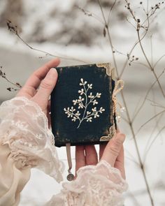 a person holding an old book in their hand with white flowers on the front cover