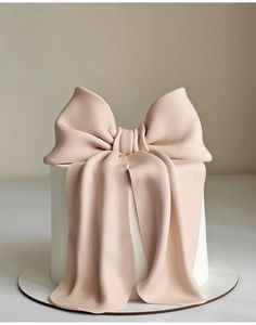 a white cake with a pink bow on it's top, sitting on a plate