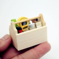 a hand holding a small wooden box filled with office supplies and magnets on it's side