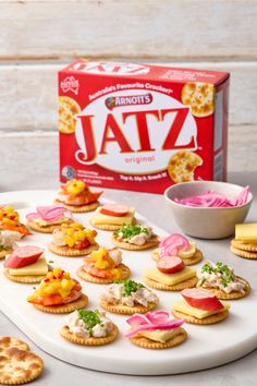 small crackers are arranged on a white platter next to a box of jam