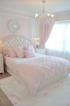 a white bed sitting in a bedroom next to a chandelier above a window