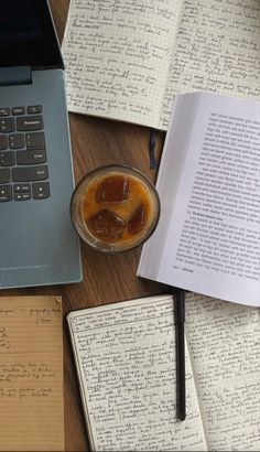 an open book sitting on top of a wooden table next to a cup of liquid