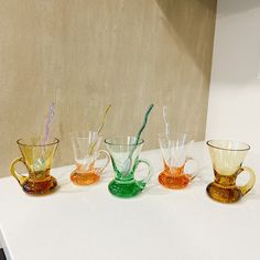 five different colored glass cups sitting on top of a white counter next to each other