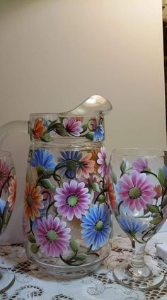 a glass pitcher and two wine glasses on a lace tablecloth with an ornate floral design