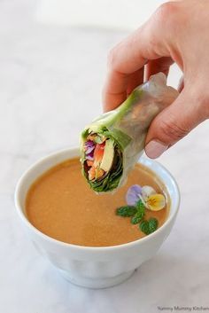 a person dipping some kind of vegetable wrap into a bowl of soup