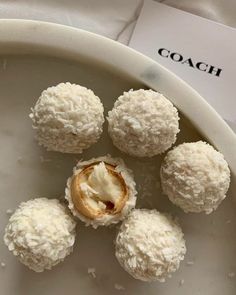 four coconut balls on a white plate with the word coach next to them