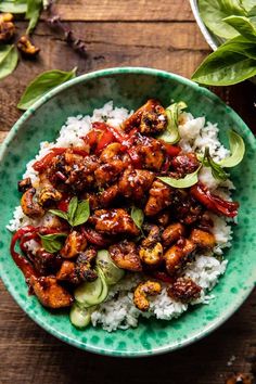 a green bowl filled with chicken and rice on top of a wooden table next to leaves