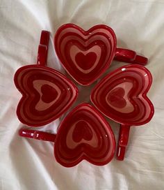 four red heart shaped dishes sitting on top of a bed