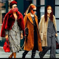 three women walking down the street with masks on their faces and one wearing a fur coat