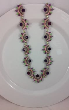 a white plate topped with a purple and green beaded necklace