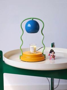 a green and white table with a blue lamp on it's top, next to a small figurine