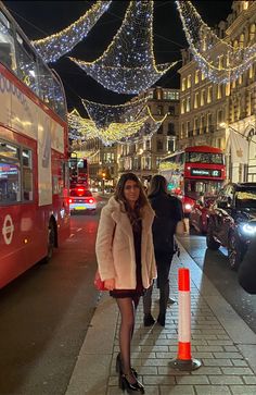 a woman is walking down the sidewalk in front of a double decker bus at night