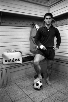 a man standing next to a soccer ball in front of a wall with adidas written on it