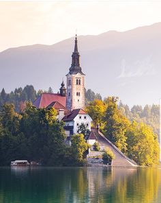 an island with a church on it in the middle of water surrounded by trees and mountains