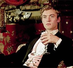 a man in a tuxedo sitting at a table with a glass of wine