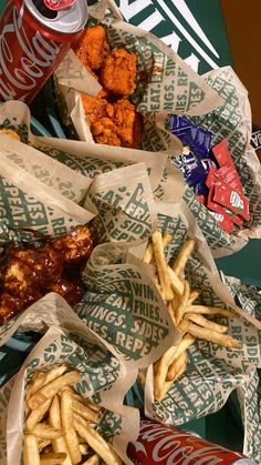 chicken wings, french fries and coca - cola are on paper wrappers next to each other