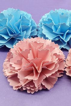 three pink and blue paper flowers sitting on top of a purple surface with one flower in the middle