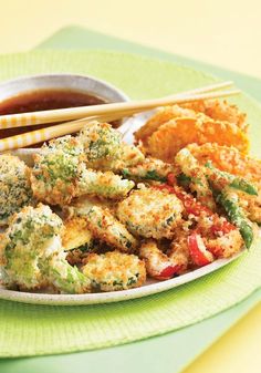 a white plate topped with fried food and chopsticks next to a bowl of dipping sauce