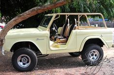 an old yellow jeep is parked in the shade under a tree with its doors open