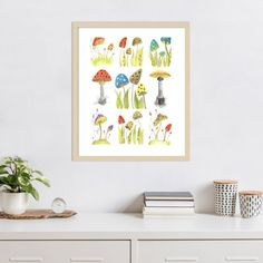 an art print of mushrooms on a white wall above a dresser with books and plants